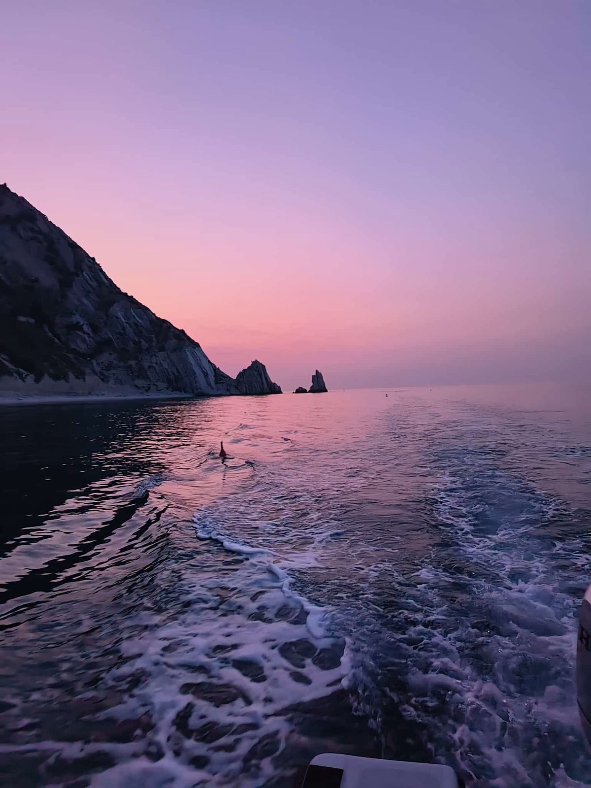 I faraglioni delle Due Sorelle al tramonto, con il mare rosa visto dalla barca