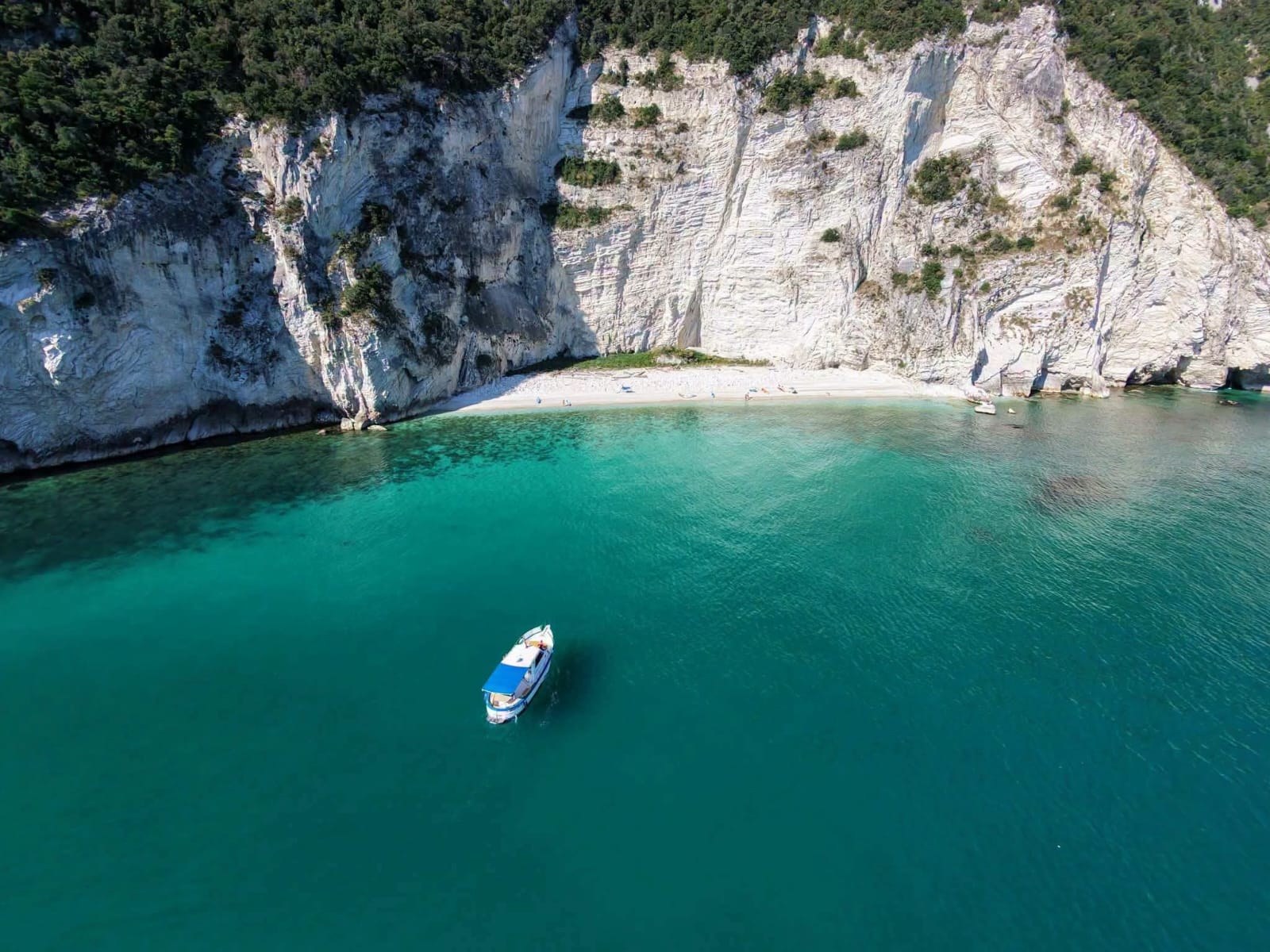 Le falesie bianche del Monte Conero a picco sul mare turchese, con una barca alla fonda