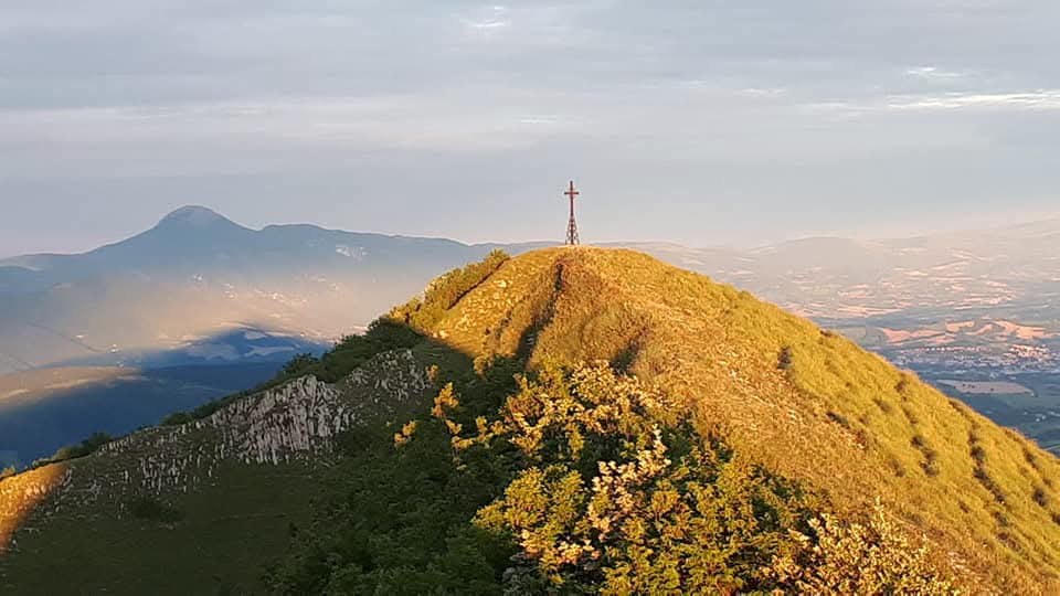 La croce di vetta su un crinale erboso dei Monti Sibillini alla luce del mattino
